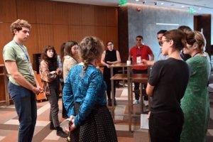 Group of adults standing around a tall table in a conference area, wearing lanyards and conversing.