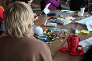 People gathered around a wooden table covered with colorful LEGO bricks, markers, notes, and a tablet during a workshop session.