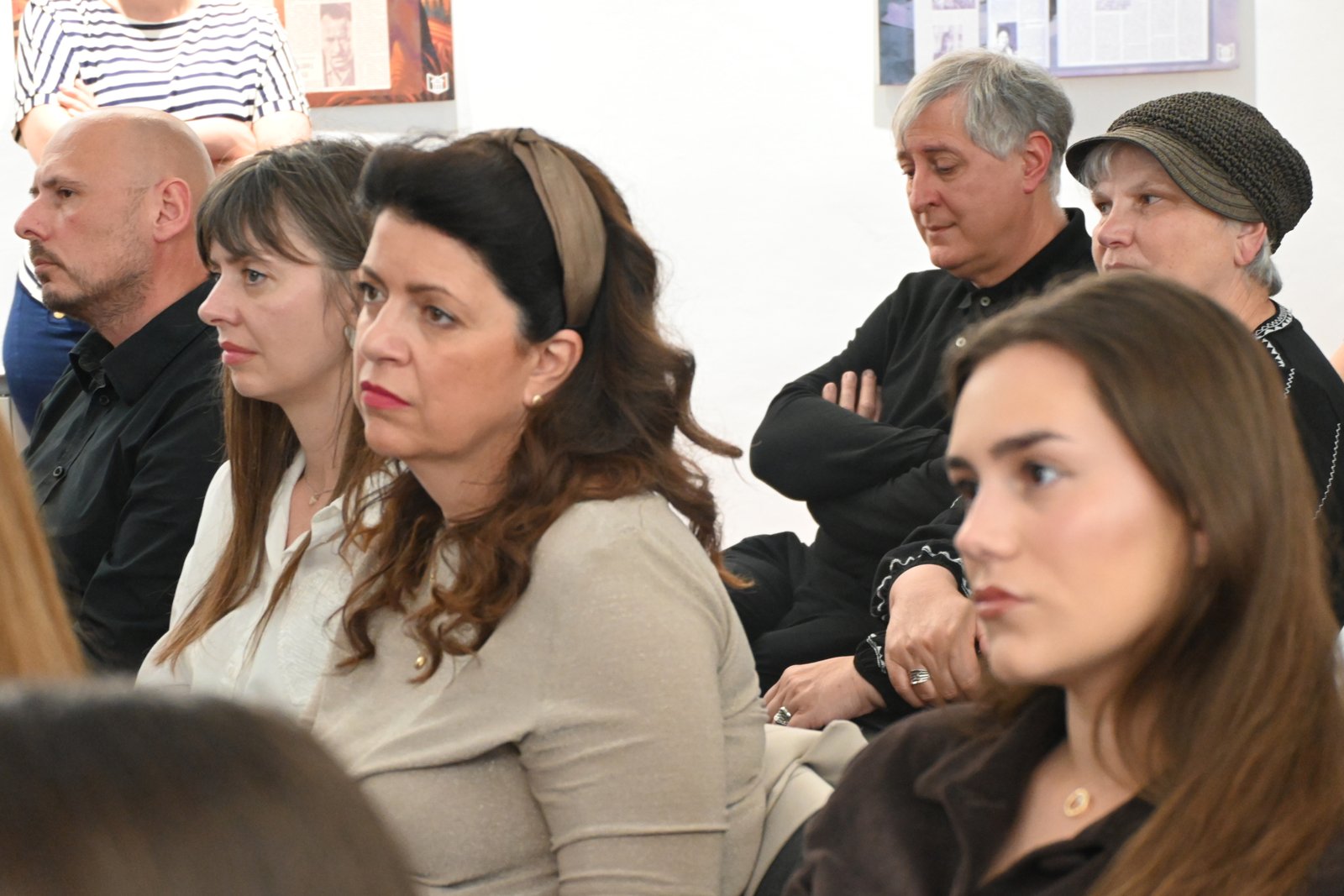 Group of adults seated indoors, facing left, listening attentively to an event off-camera.