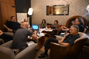 Group of people seated around a coffee table in a cozy lounge, working with laptops, papers, and bottles of water gathered for a meeting.