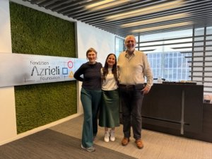 Three coworkers pose and smile in a modern office lobby with a moss wall and the Azrieli Foundation sign in the background.