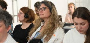 Group of people wearing headsets, seated and listening attentively in a workshop or classroom.