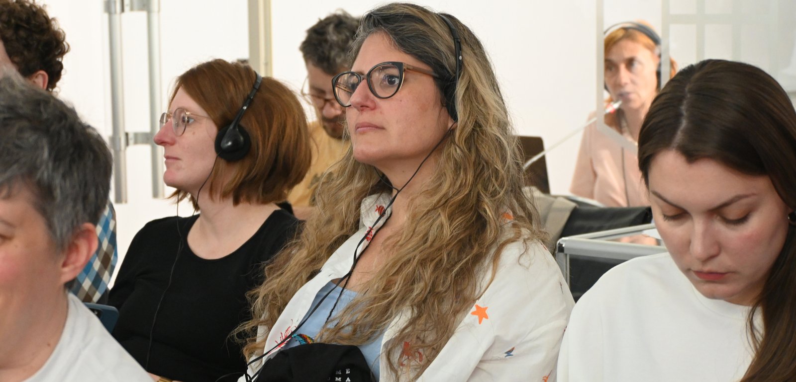 Group of people wearing headsets, seated and listening attentively in a workshop or classroom.