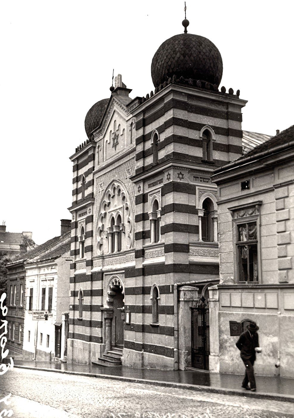 Historic striped building with onion domes and arched windows on a cobblestone street; a person walks by.