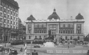 Historic Belgrade plaza with a large domed bank building, a central statue, and tram in the foreground—classic early 20th‑century street scene