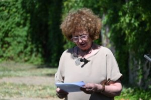 Older woman with curly brown hair and glasses reads papers outdoors in a sunny park setting