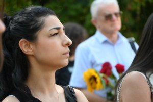 Profile of a young woman at an outdoor event, with a bouquet of flowers blurred in the background.