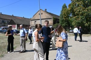 Group of casually dressed people chatting outside weathered brick buildings on a sunny day under a clear blue sky.