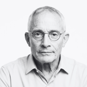 Close-up portrait of an older man with round glasses looking straight ahead.